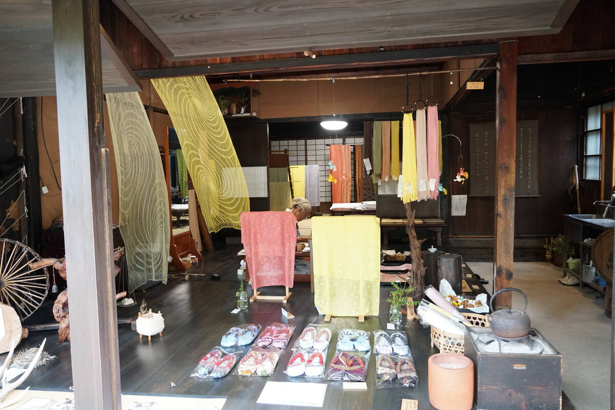 Inside a traditional textile shop in Tsumago, bolts of indigo and colorful fabrics hang from wooden beams, crafts displayed on the floor