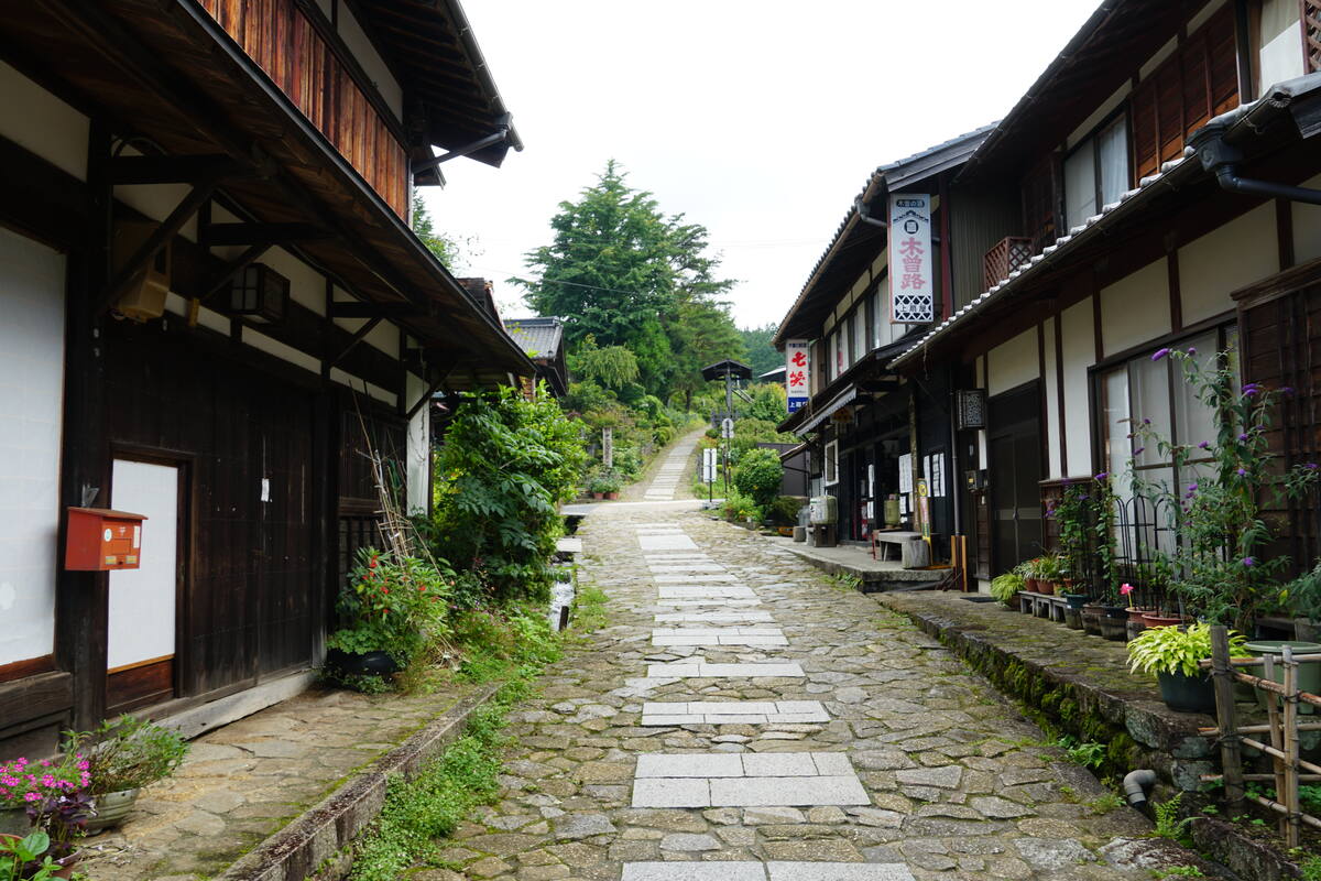 Traveler walking the stone-paved main street of Tsumago with traditional timber buildings and valley mountains in view