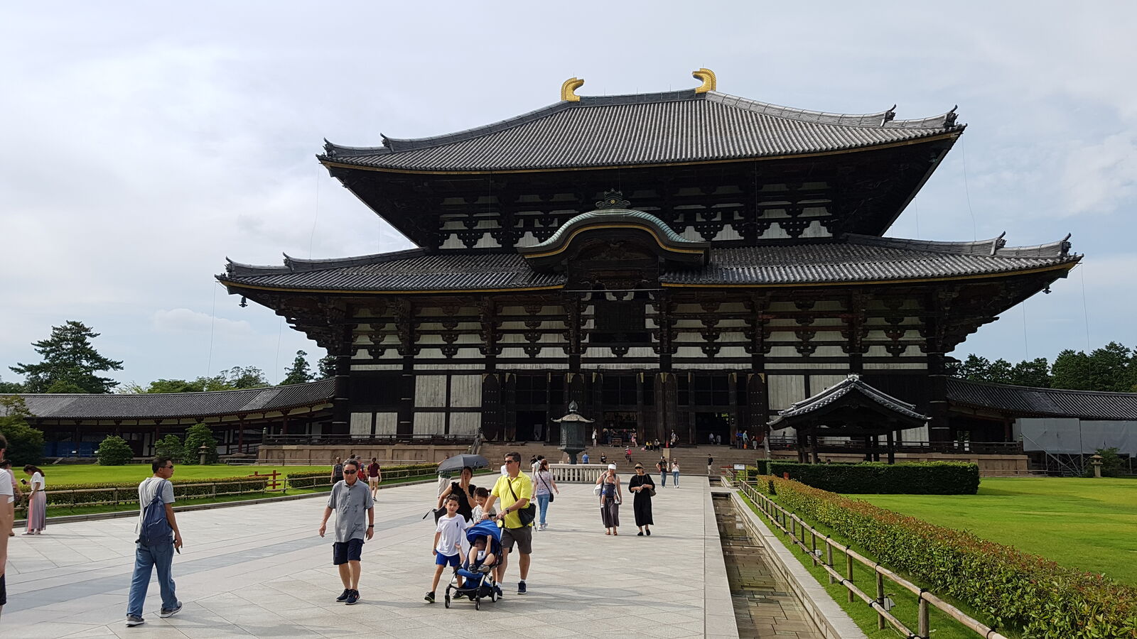 The frontal approach to Todai-ji, visitors walking toward the enormous wooden hall, the sheer scale of the building becoming apparent as people shrink against its facade