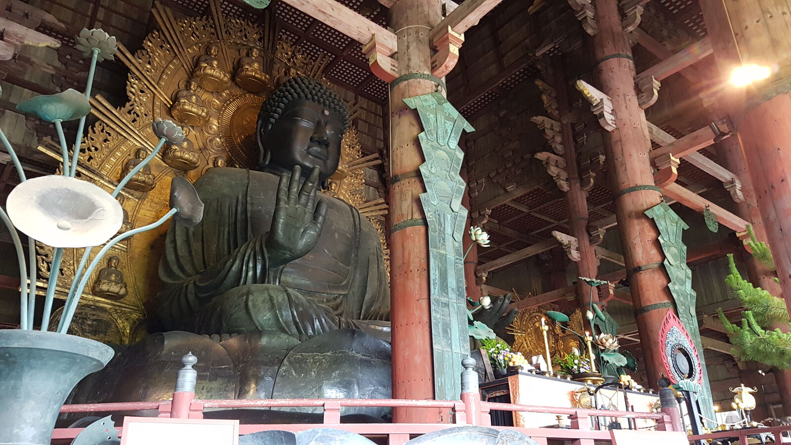 The Great Buddha of Todai-ji, the enormous bronze Daibutsu seated in meditation, lotus flower offerings and ornate golden halo behind, massive wooden pillars framing the fifteen-meter statue