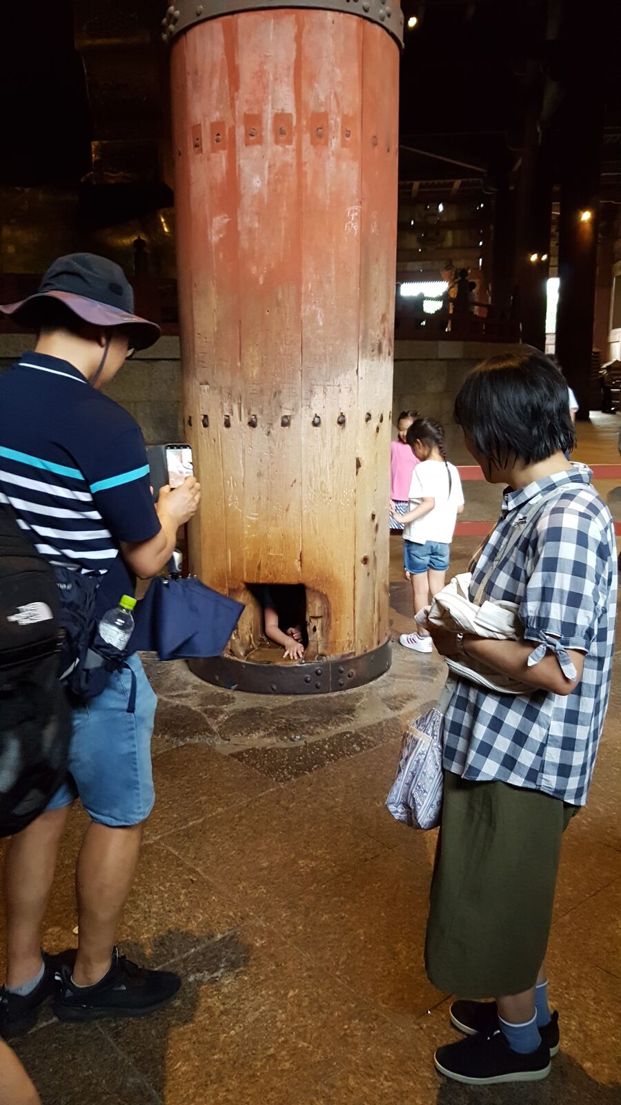 A person squeezing through the famous pillar hole at Todai-ji, the opening said to be the same size as the Great Buddha's nostril, onlookers watching and cheering