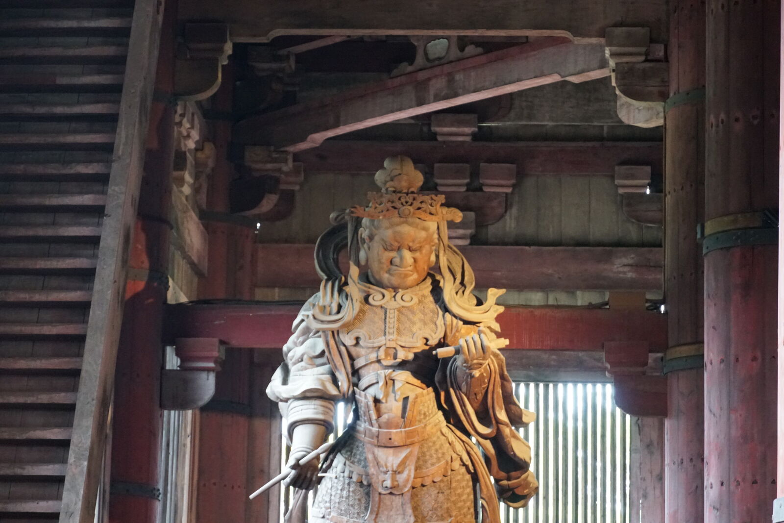 A wooden guardian statue inside Todai-ji, the fierce Komokuten figure carved in dramatic detail, lit from behind by window light