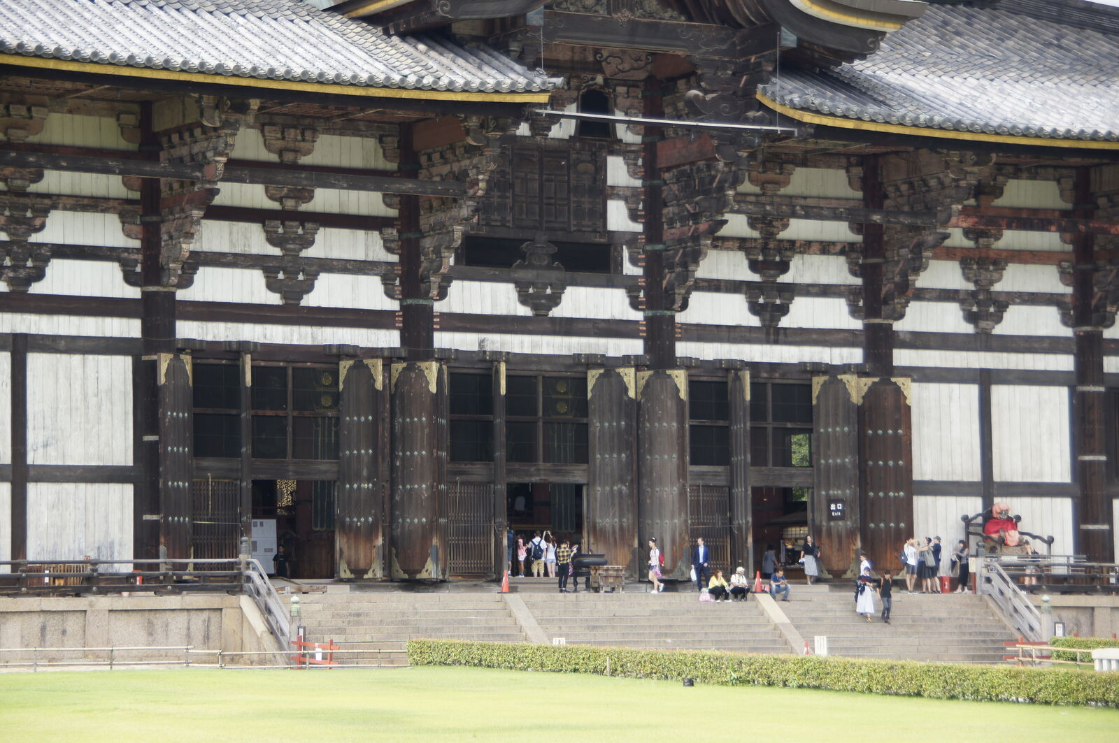 Detail of Todai-ji's facade: the intricate wooden bracket system supporting the enormous roof, visitors visible at the base giving a sense of the building's towering scale