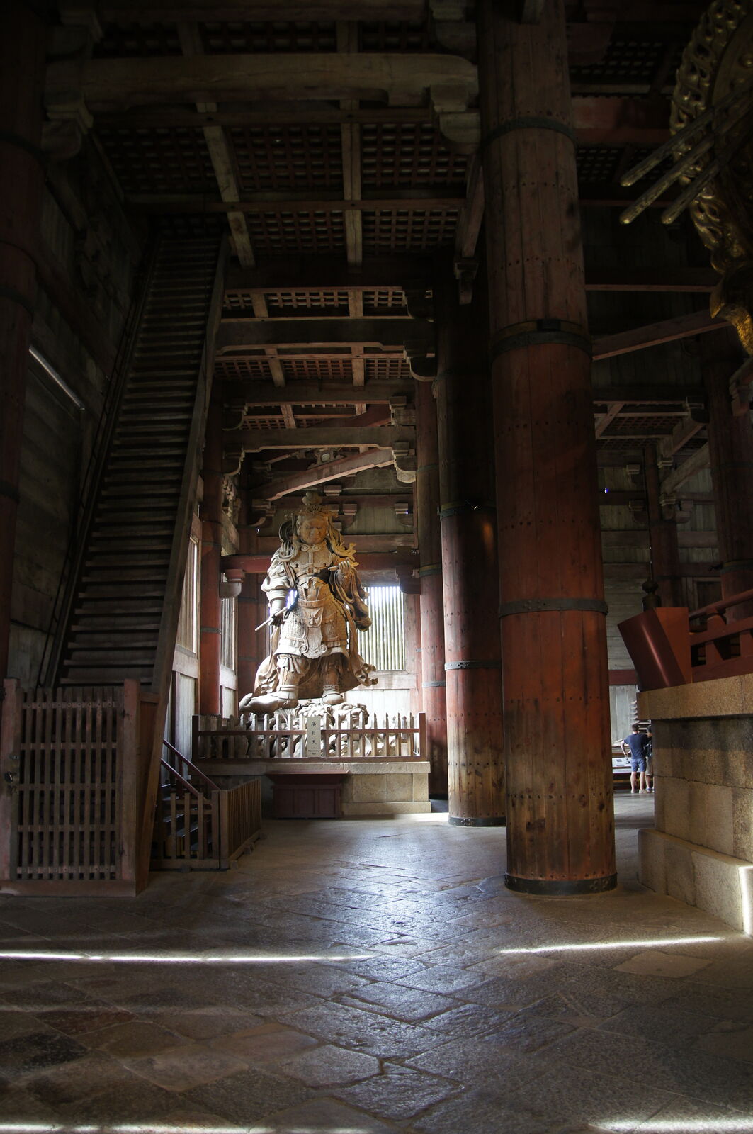 Looking straight up inside Todai-ji at the wooden ceiling structure, a guardian figure visible between the massive beams, the engineering of the eighth century on full display