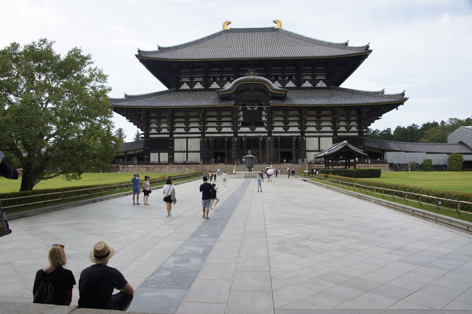 Todai-ji from the main approach path, a couple sitting on the stone edge in the foreground, the massive building filling the frame behind them