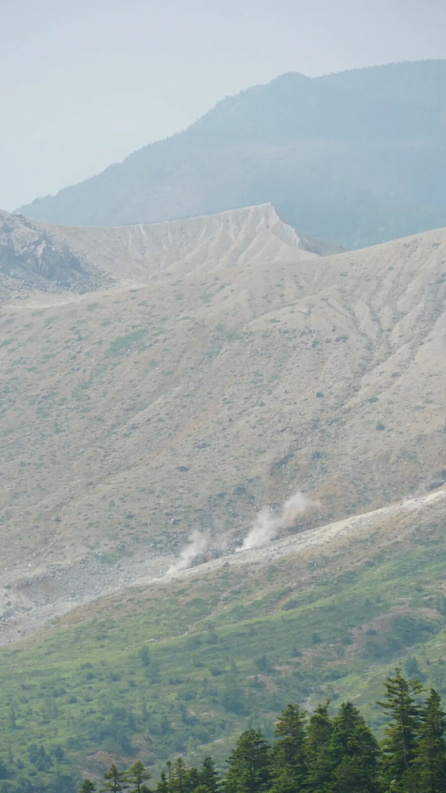 Volcanic fumaroles releasing steam on the barren mountainside of Kusatsu-Shirane, wisps of white against grey rock