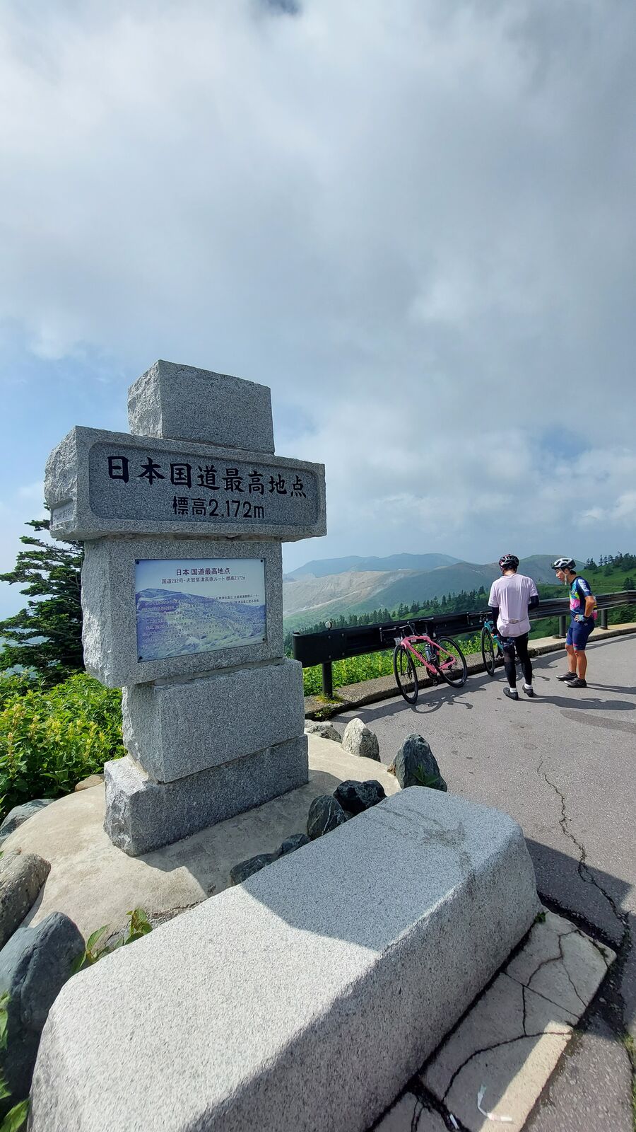 Cyclist posing at the highest point monument after completing the climb, bicycle leaning against the stone