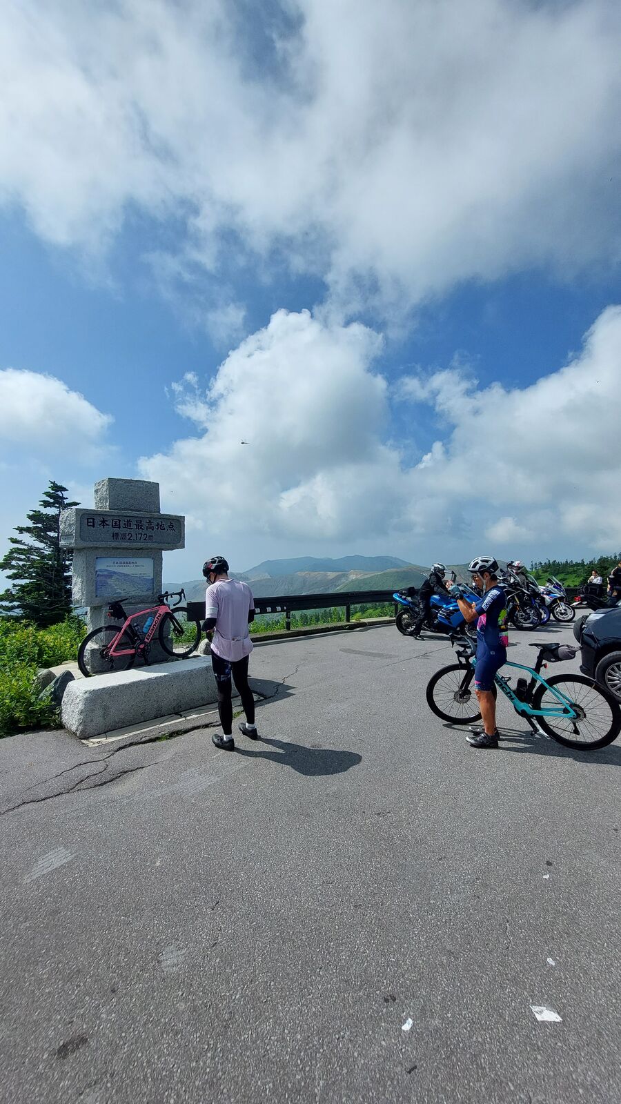 Cyclists gathering at the highest point monument after completing the climb, bicycles and mountain backdrop