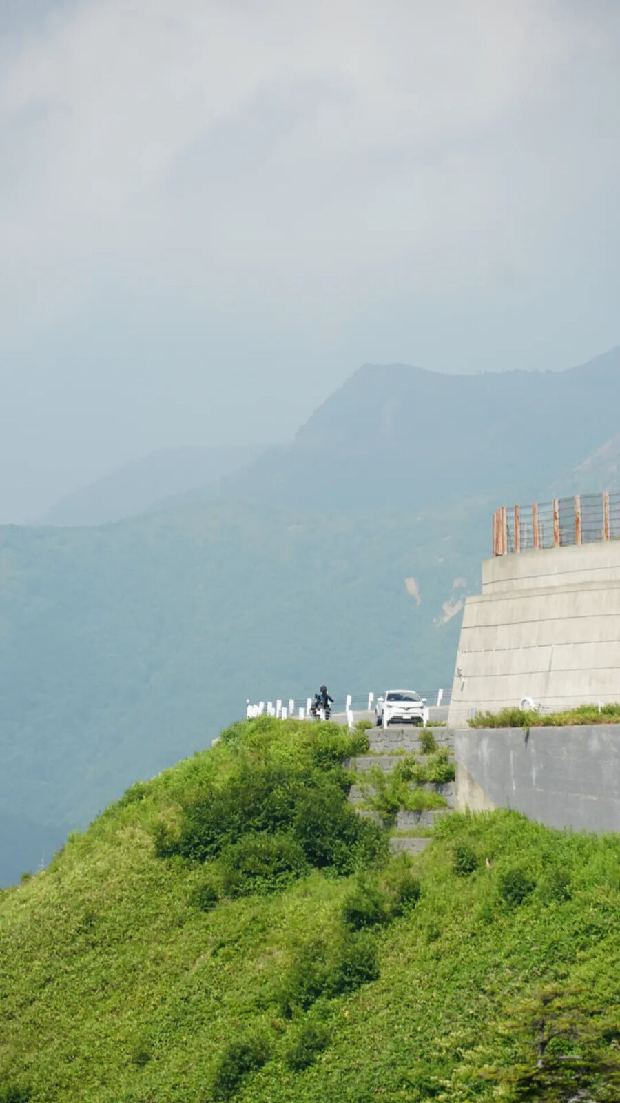 Motorcycle and car on the mountain ridge road with layers of mountains fading into haze behind them
