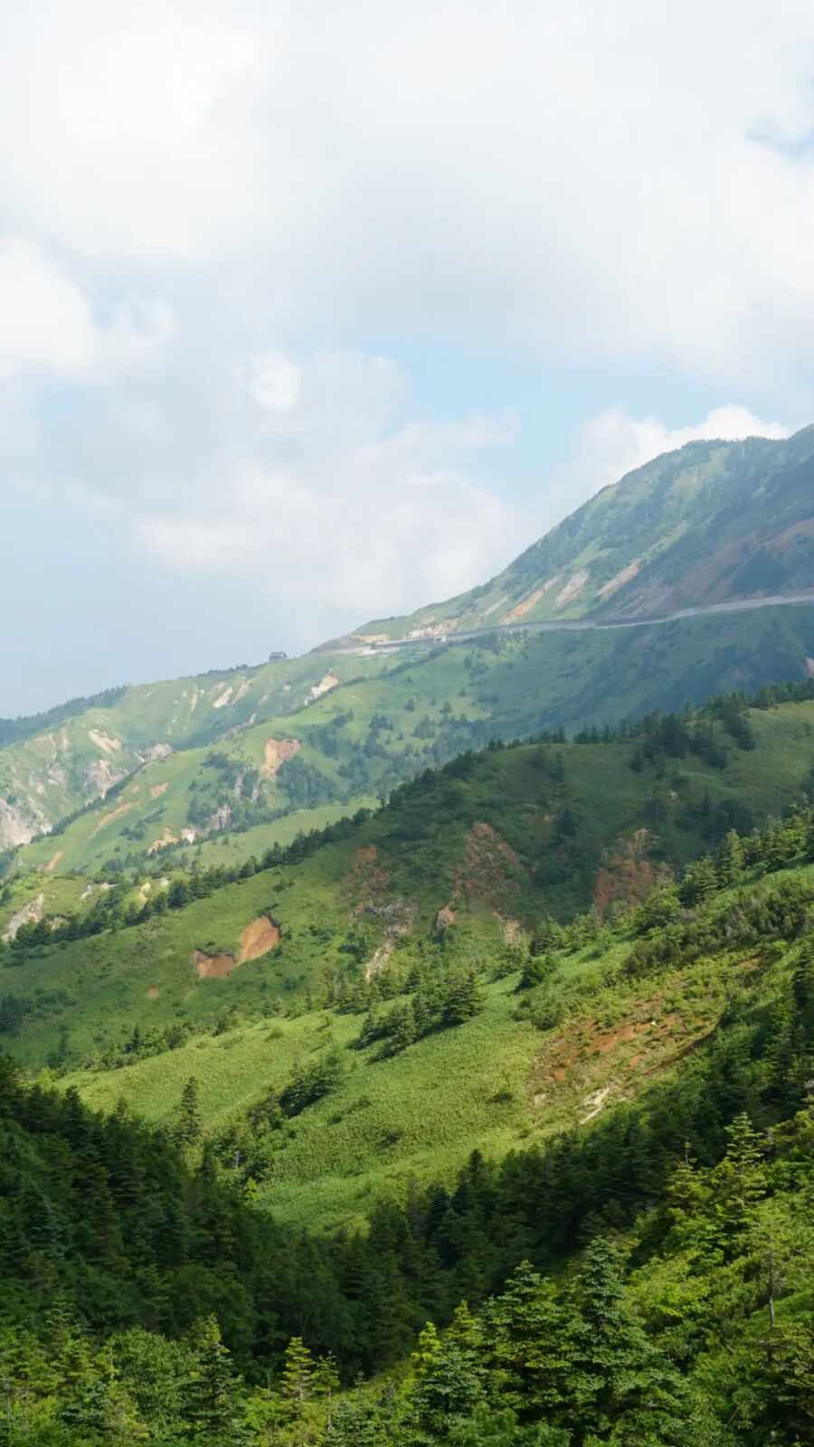 Mountain slopes with the road visible zigzagging up through forest and alpine terrain toward the summit