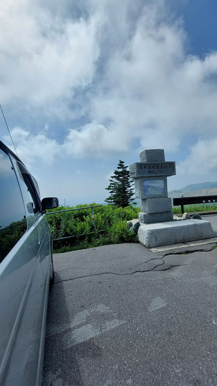 Campervan parked next to the highest point monument at 2,172 meters, dramatic clouds and mountain peaks behind