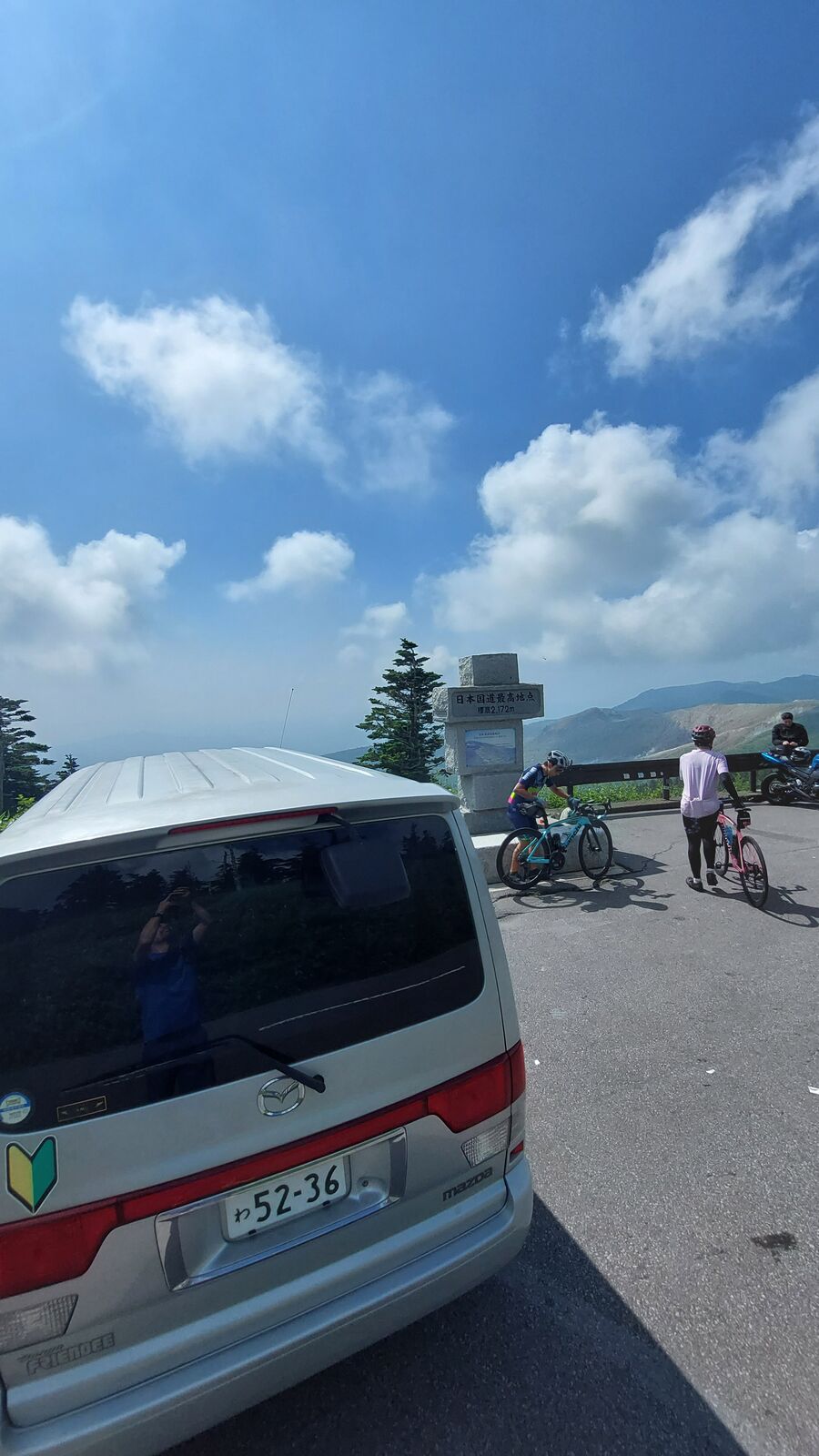 Wide view of the campervan and monument with cyclists and mountain backdrop
