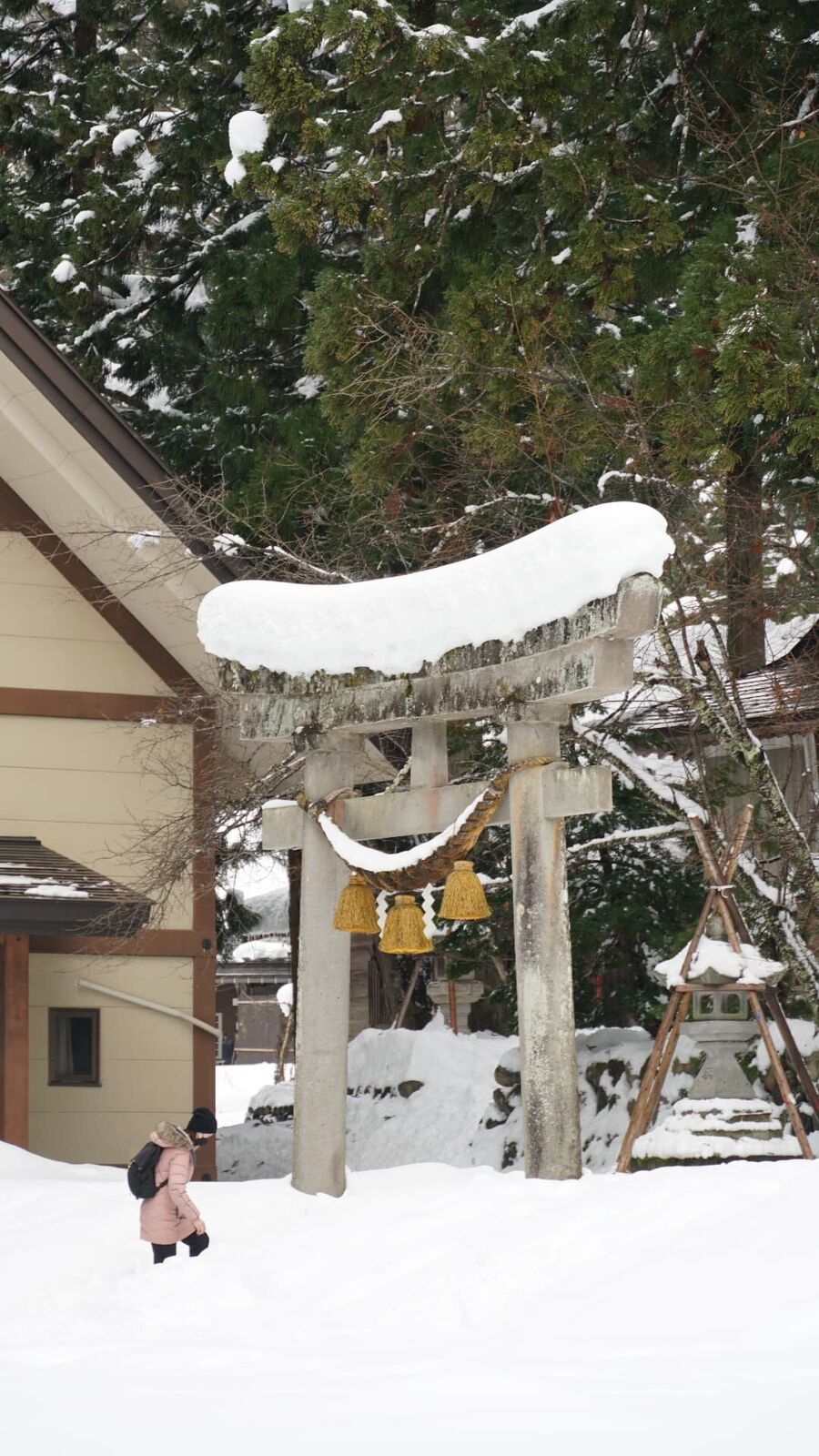 Visitor walking through a snow-covered stone torii gate with Gassho houses behind