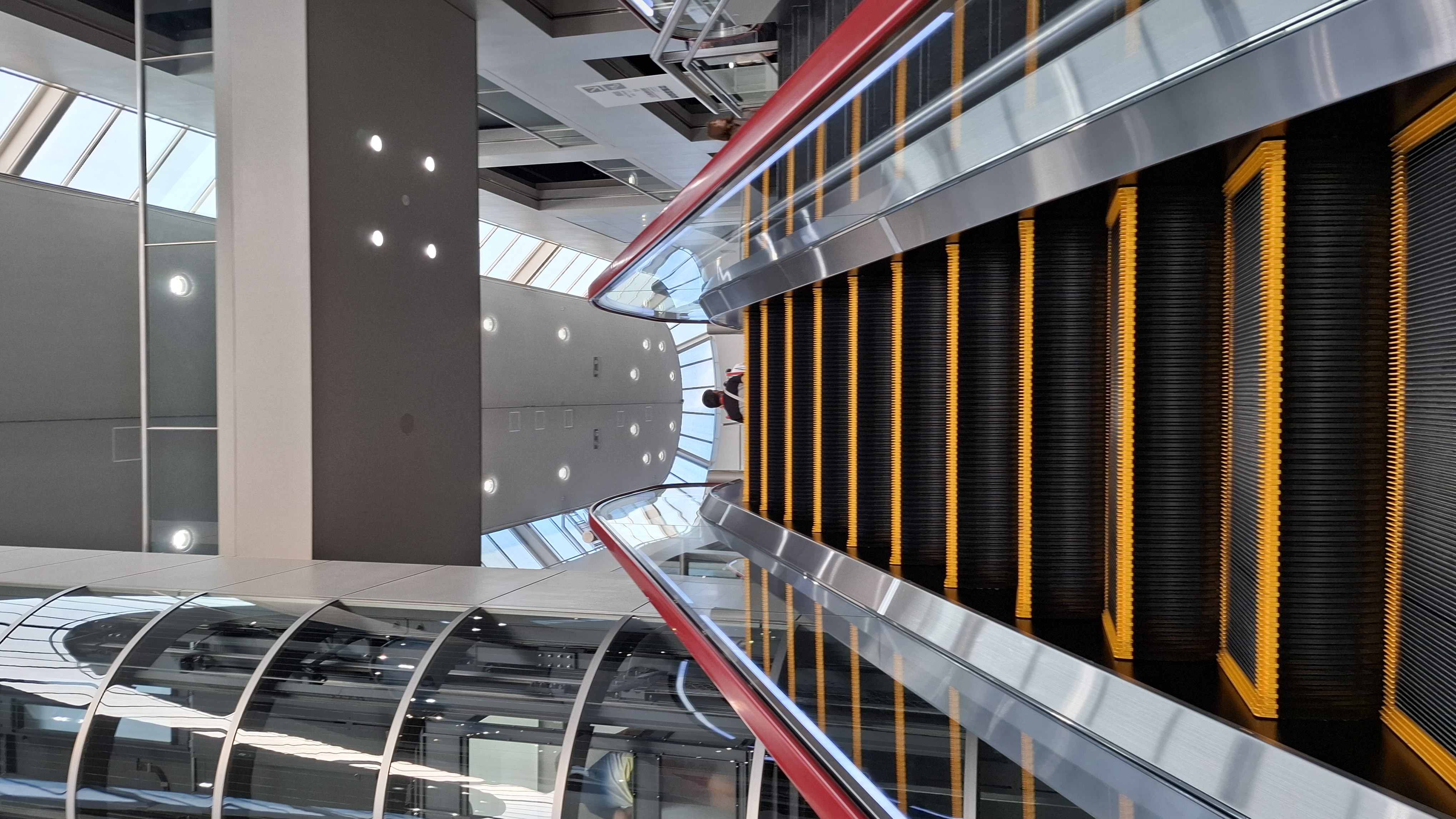 Museum interior architecture: red escalator, yellow accent panels, glass and steel atrium