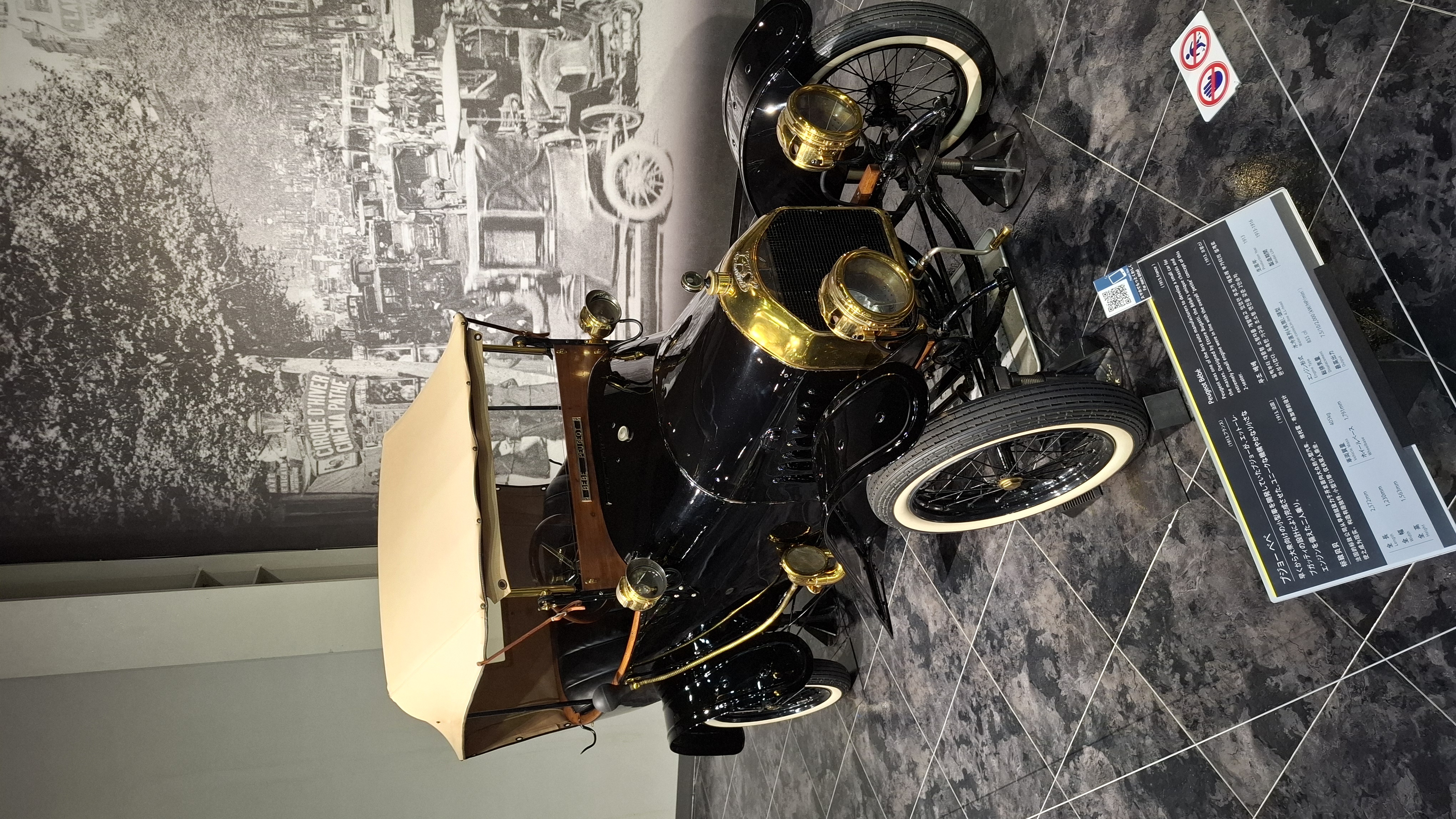 Black Ford Model T with brass headlamps and whitewall tires, factory photograph behind