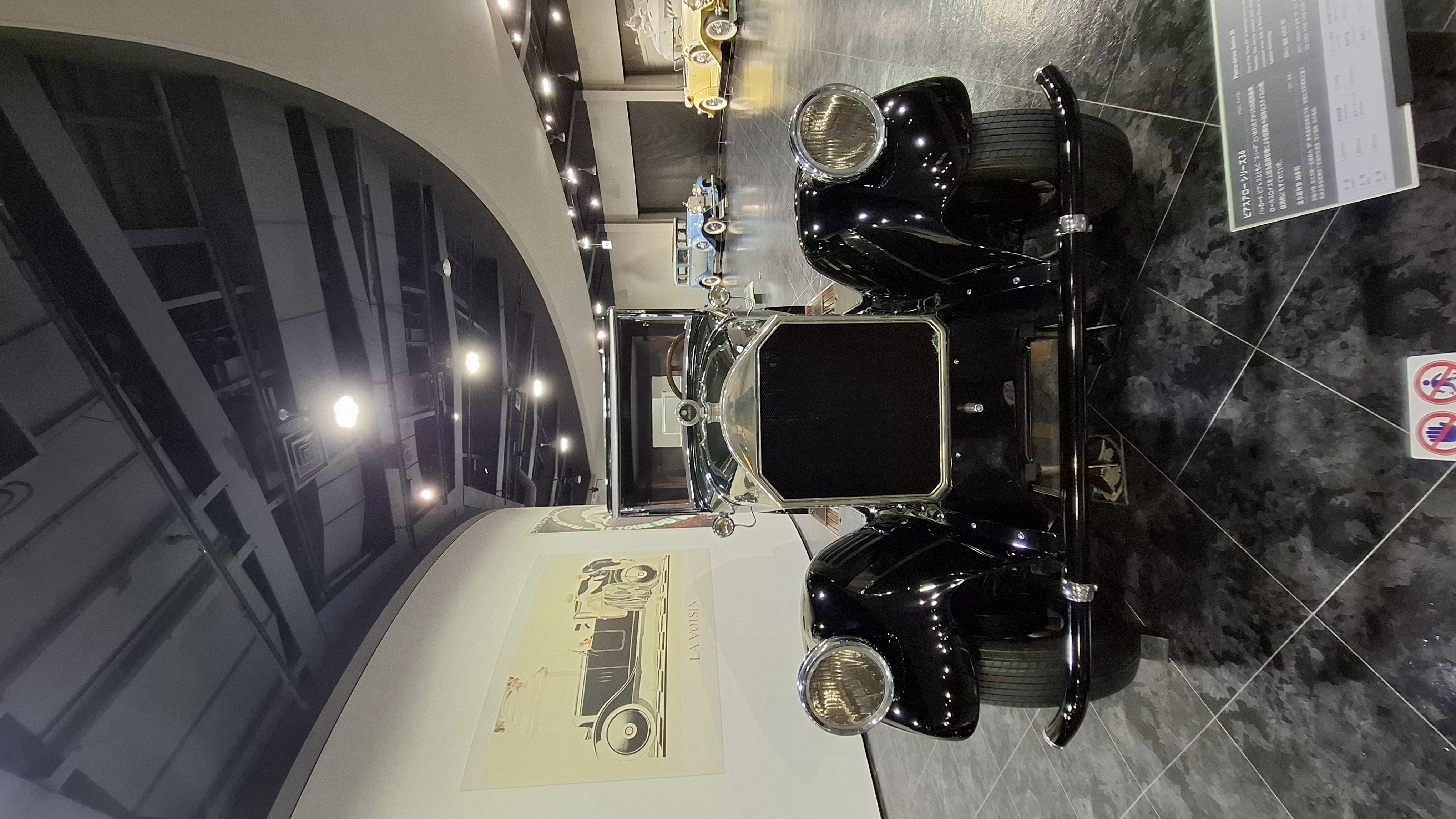 Black 1920s sedan with chrome accents and period advertising poster on the wall