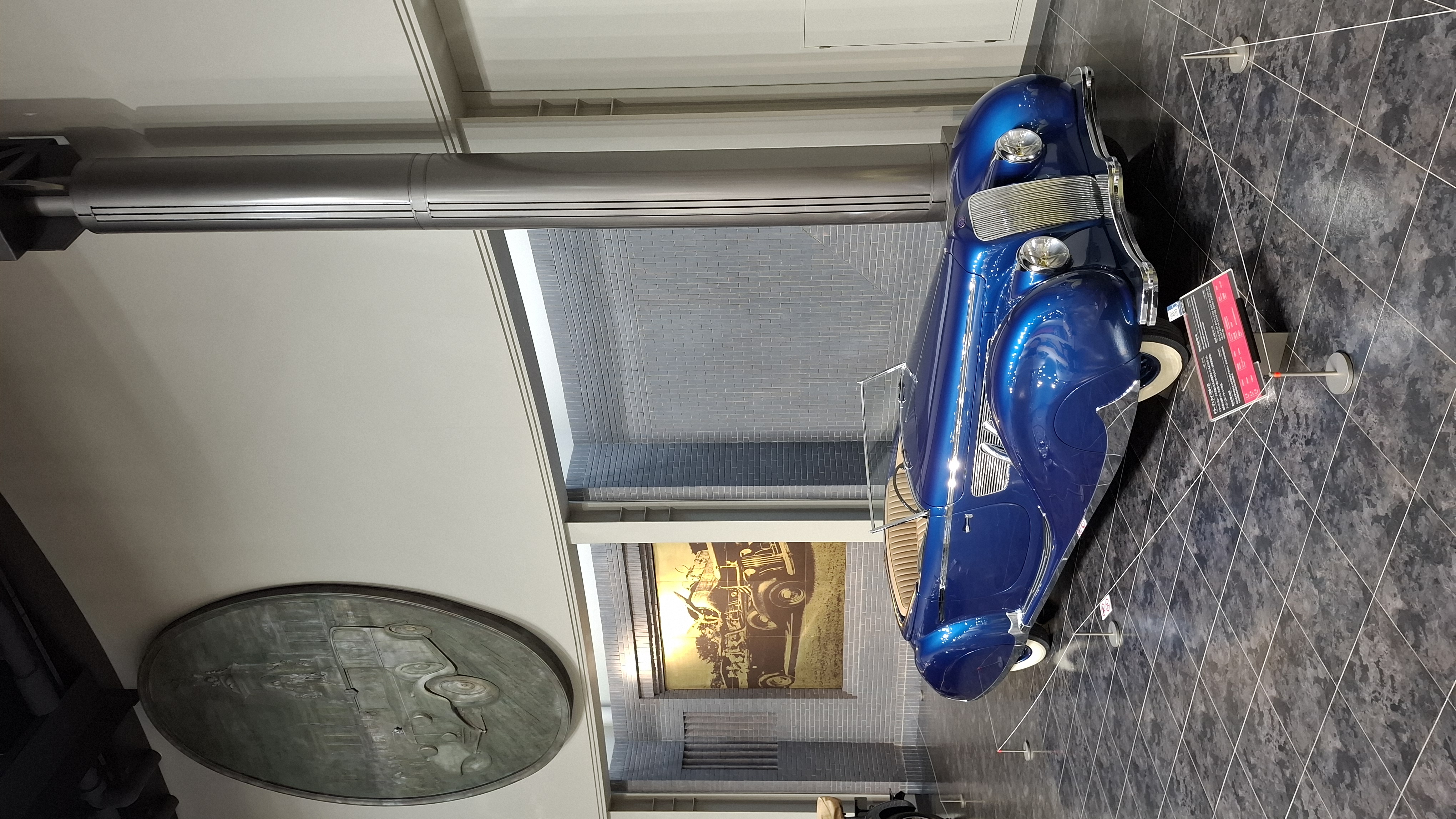 Delahaye 135MS from above, the blue paint and tan interior visible, bronze relief medallion on the wall behind