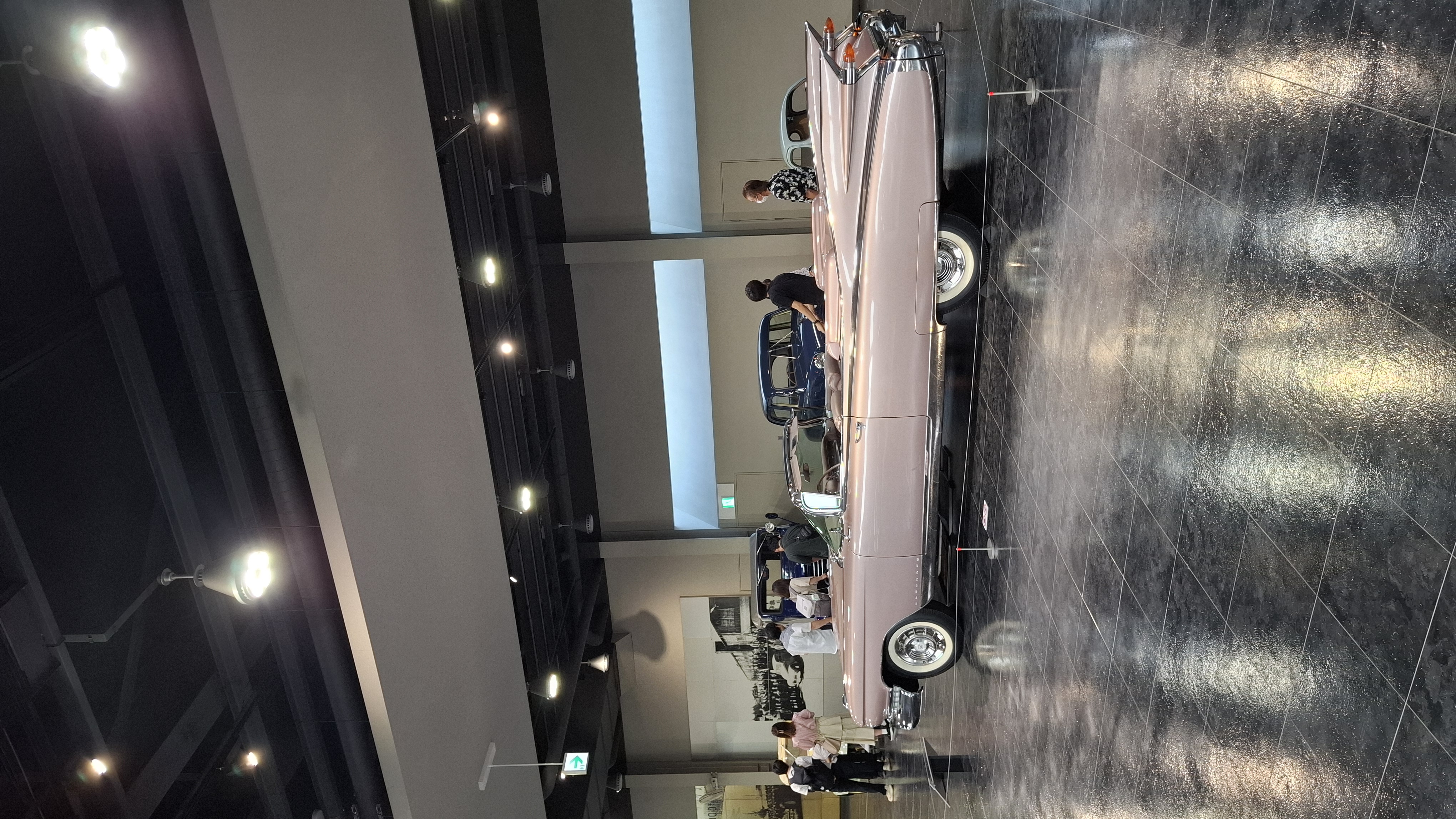 Pink Cadillac Eldorado from the side, the absurd length and chrome fins stretching across the museum floor