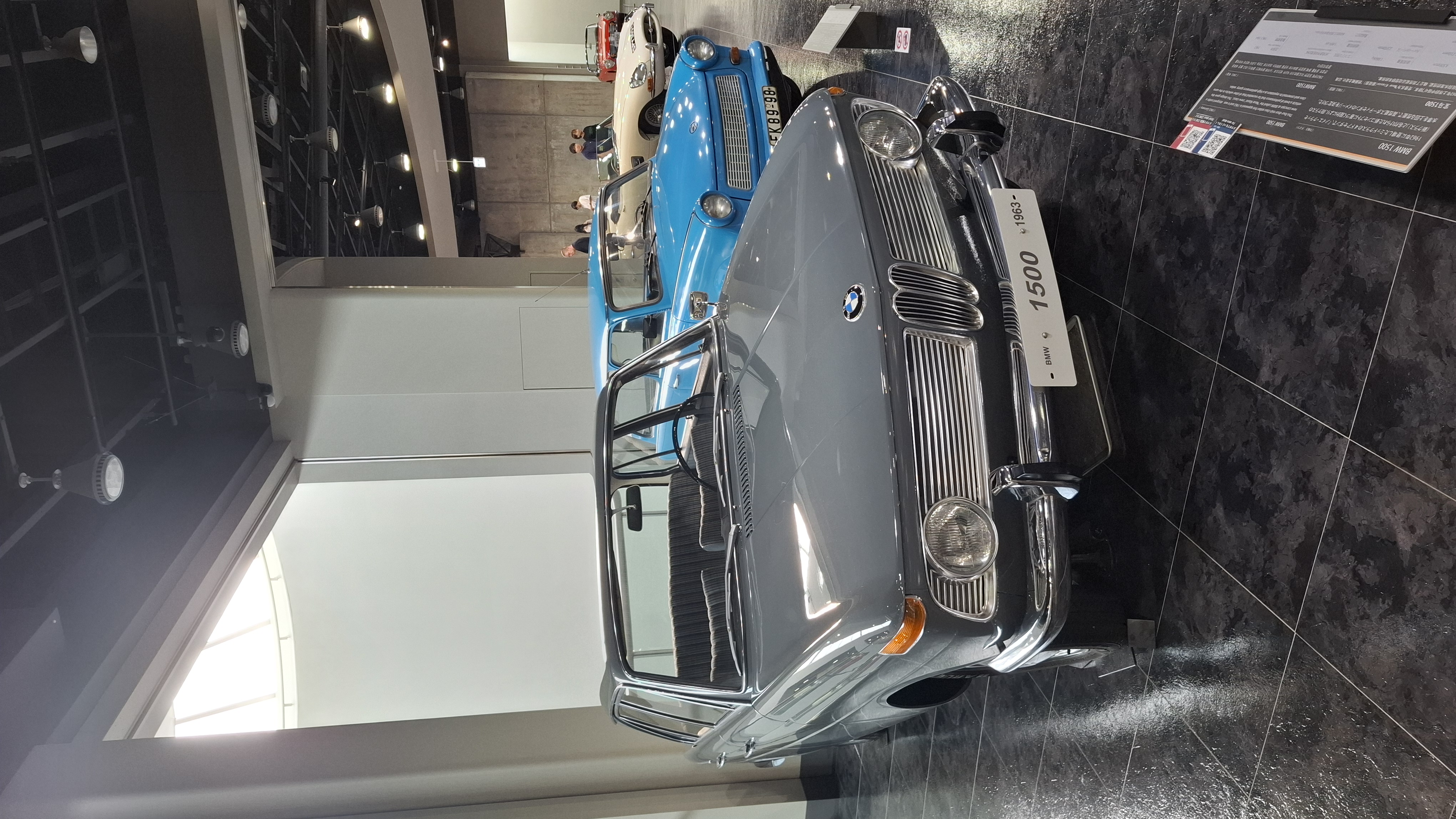 BMW 1500 with a light blue Trabant hiding just behind it, capitalism and communism side by side