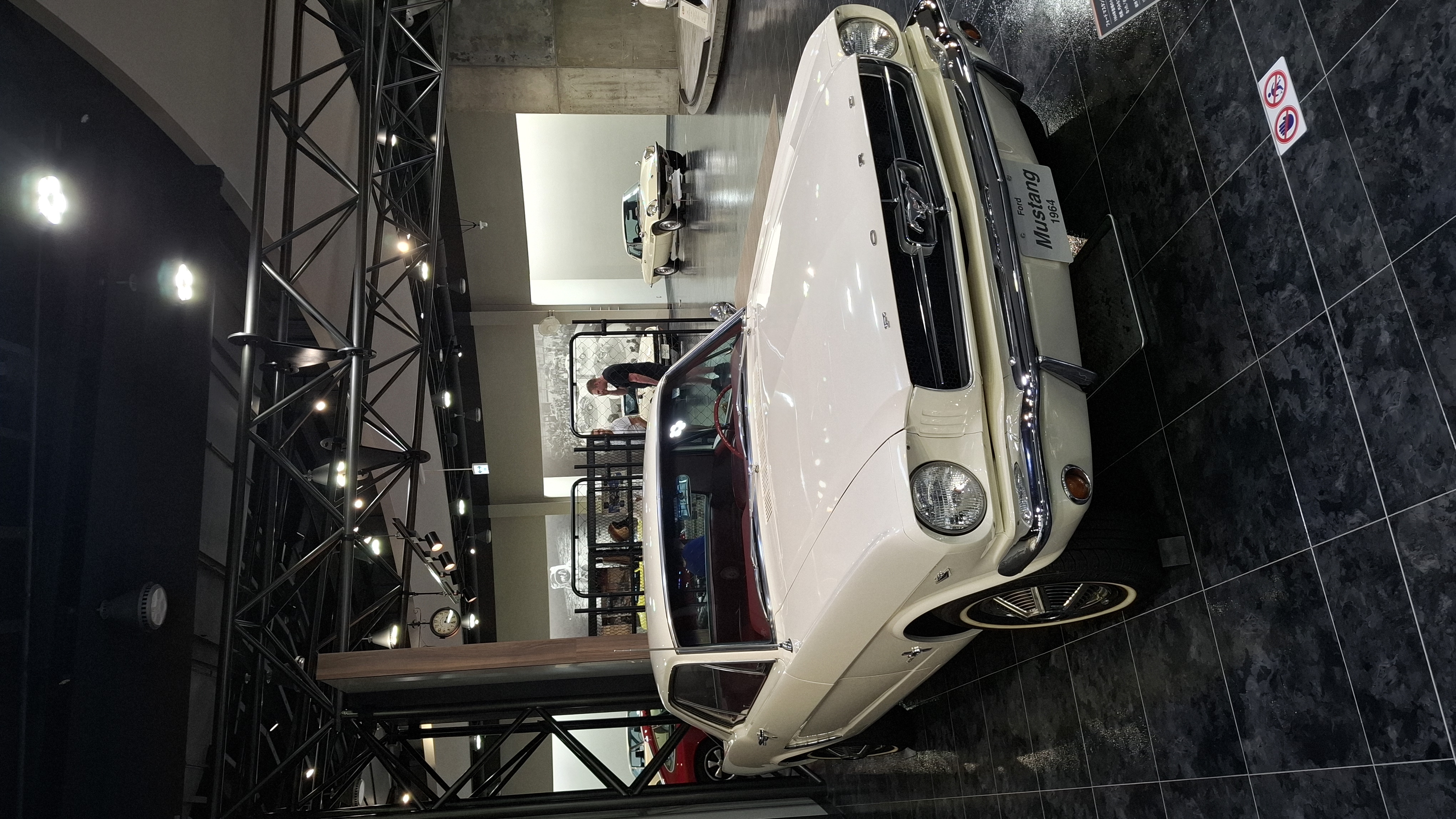 Full view of the white Mustang on the museum floor, period racing photograph behind