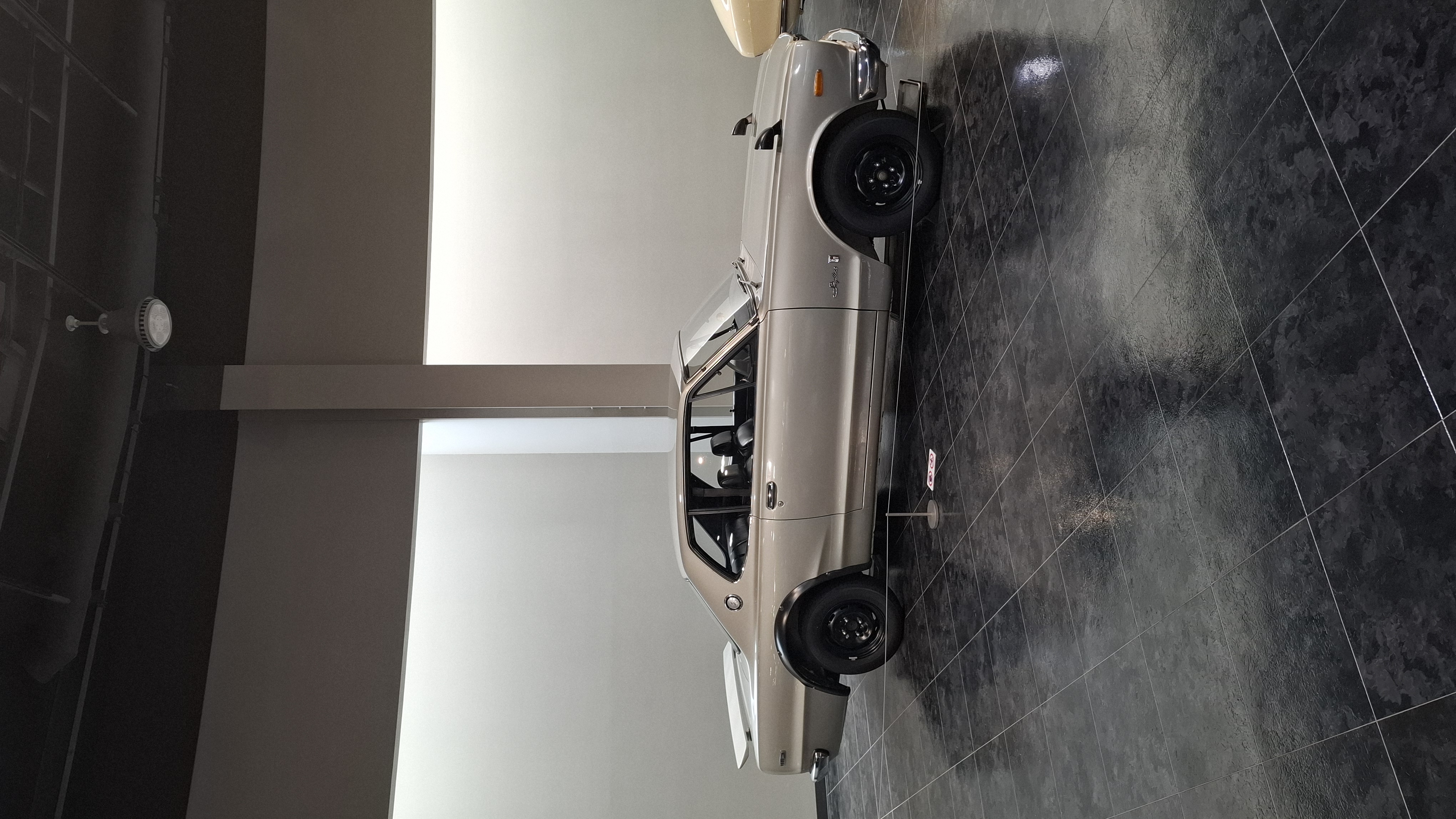 Hakosuka GT-R full side view from phone camera, silver paint gleaming on the dark floor