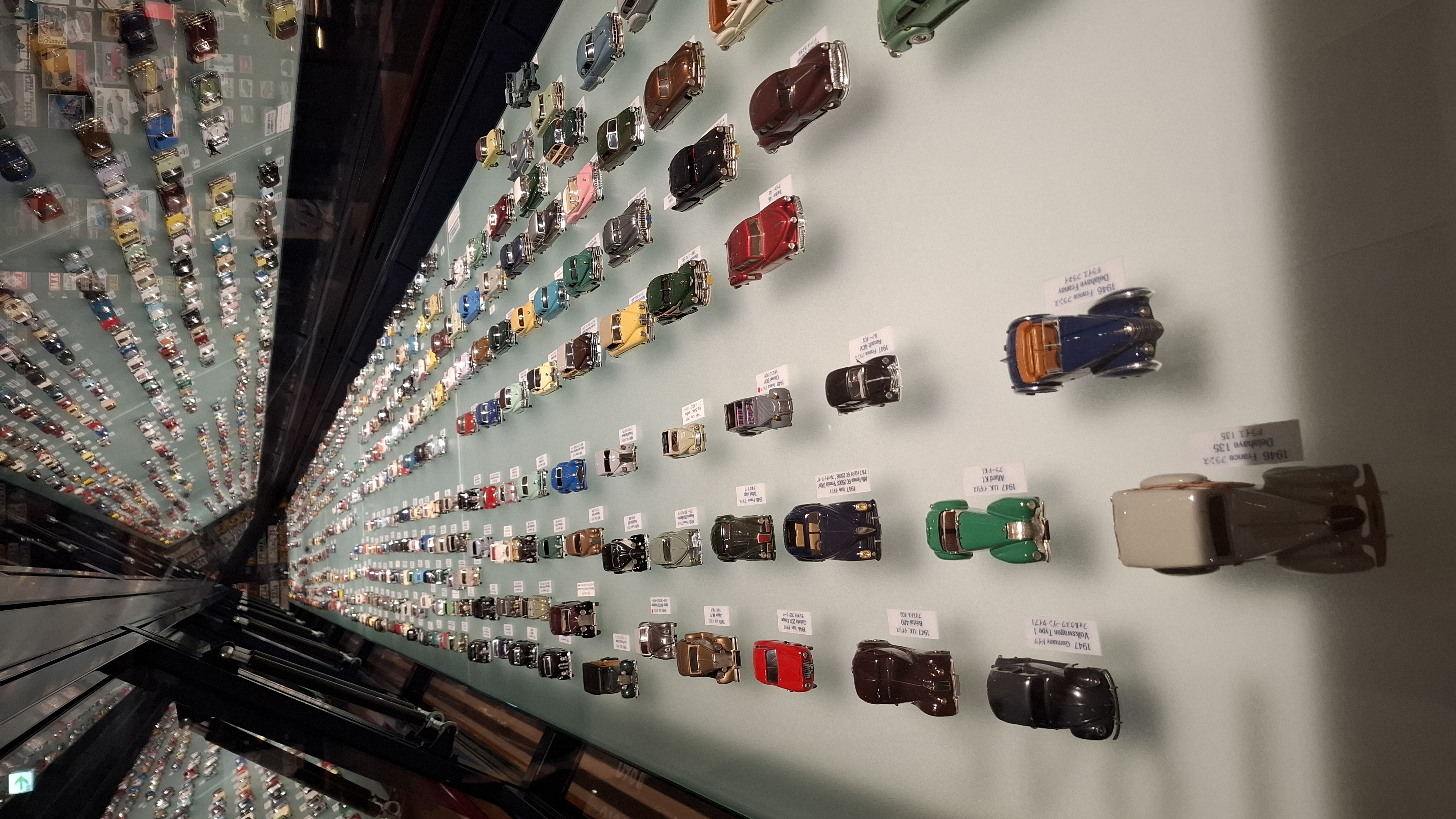 Wall of hundreds of scale model cars arranged in rows, every color and era represented, a museum within a museum
