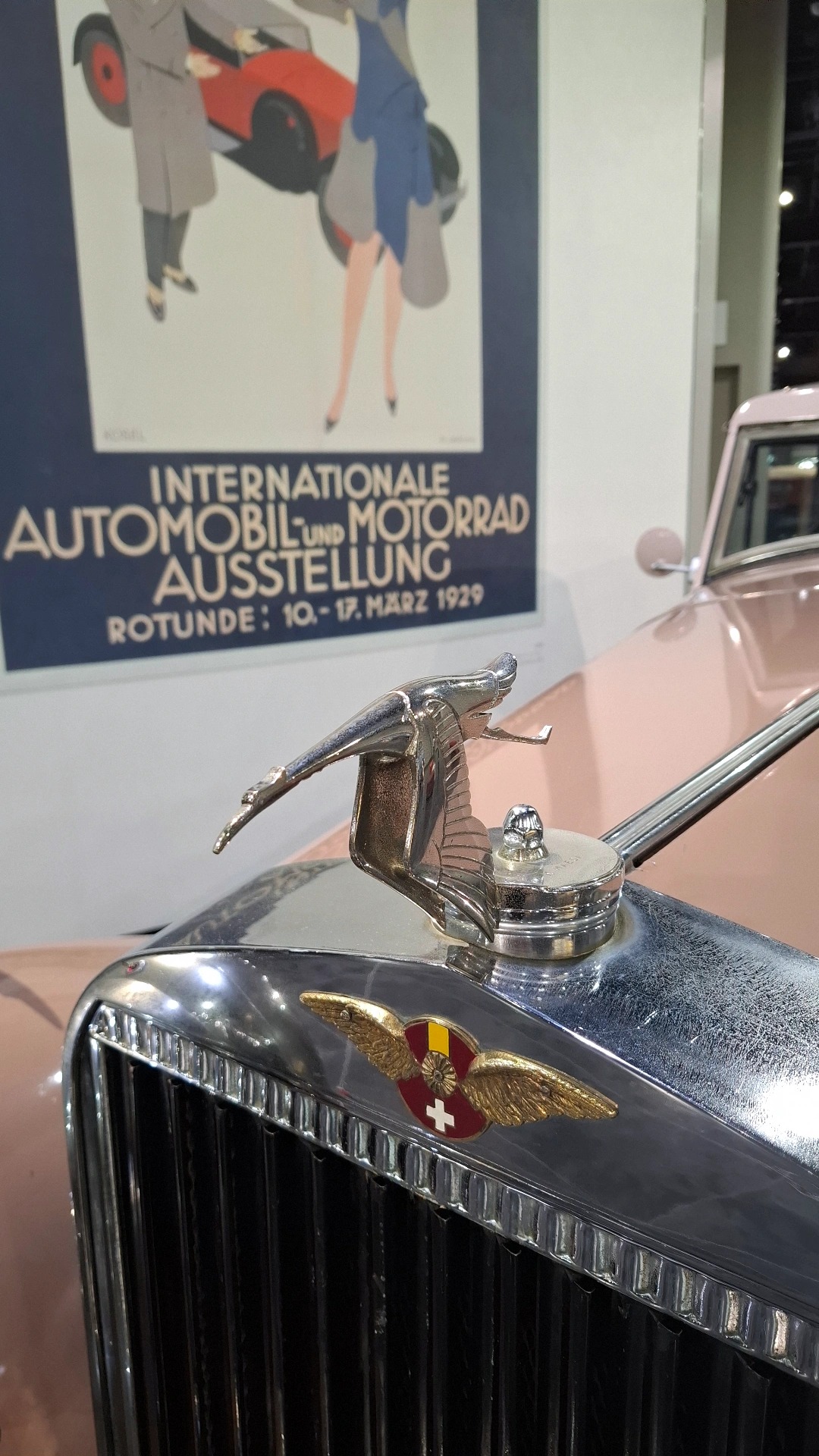 Hispano-Suiza flying stork hood ornament with Swiss coat of arms, 1929 auto show poster in background