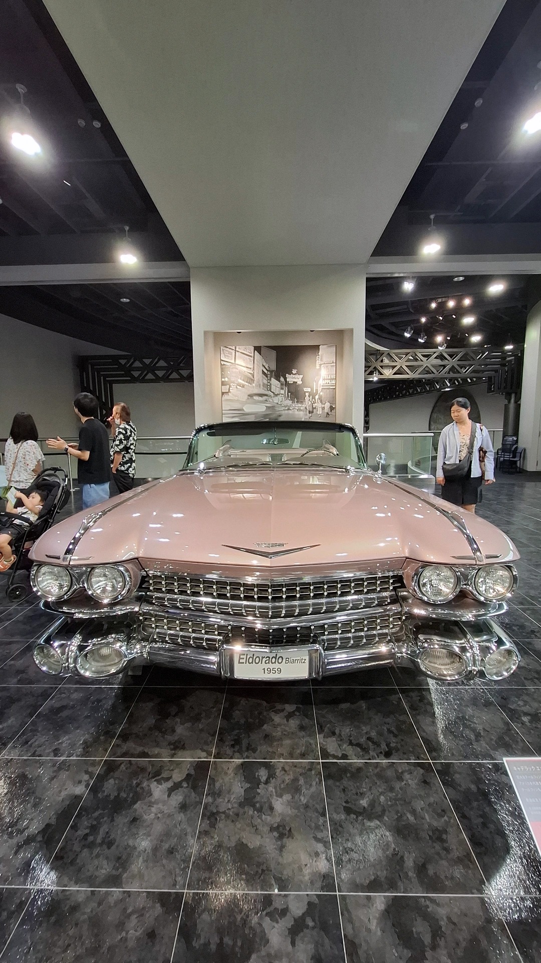 1959 Cadillac Eldorado in pink, front view with massive chrome bumper and dual headlights, visitors in awe