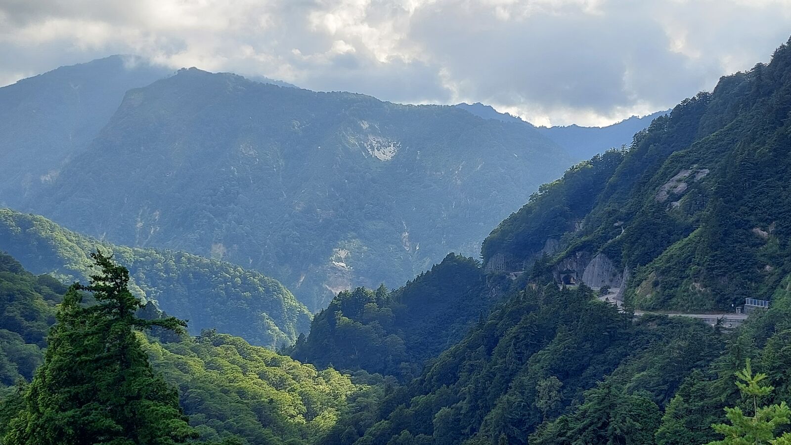 Mountain ridges layered in atmospheric perspective, shafts of light breaking through clouds onto the slopes