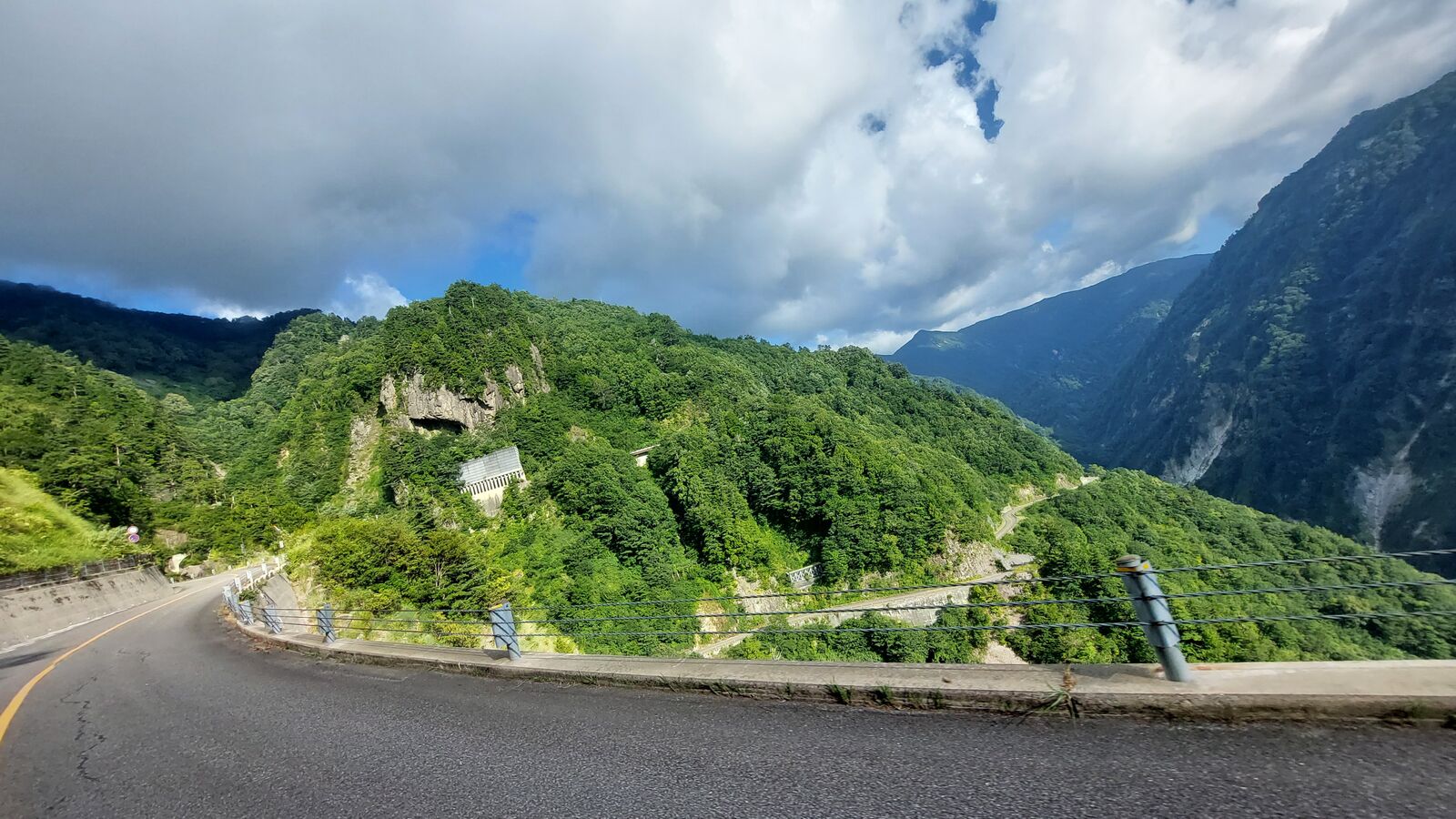 Road sweeping into a wide curve with a tunnel carved into the cliff face, deep green vegetation covering the mountainside
