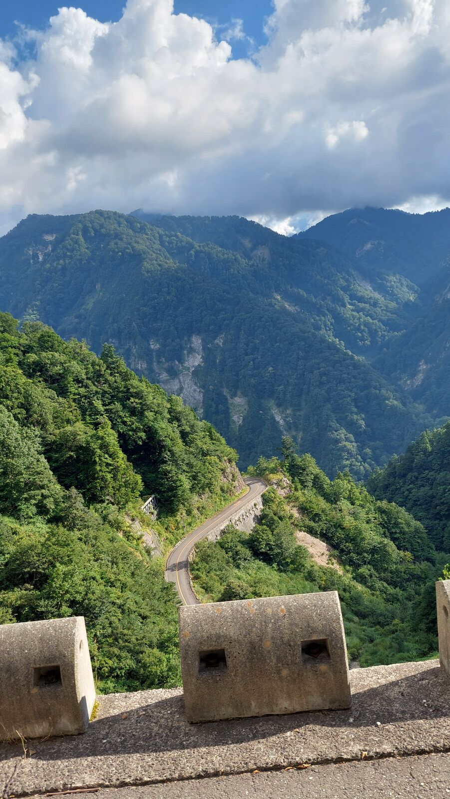 The mountain road seen from above with volcanic shelters visible along the cliff wall, switchbacks descending into the valley