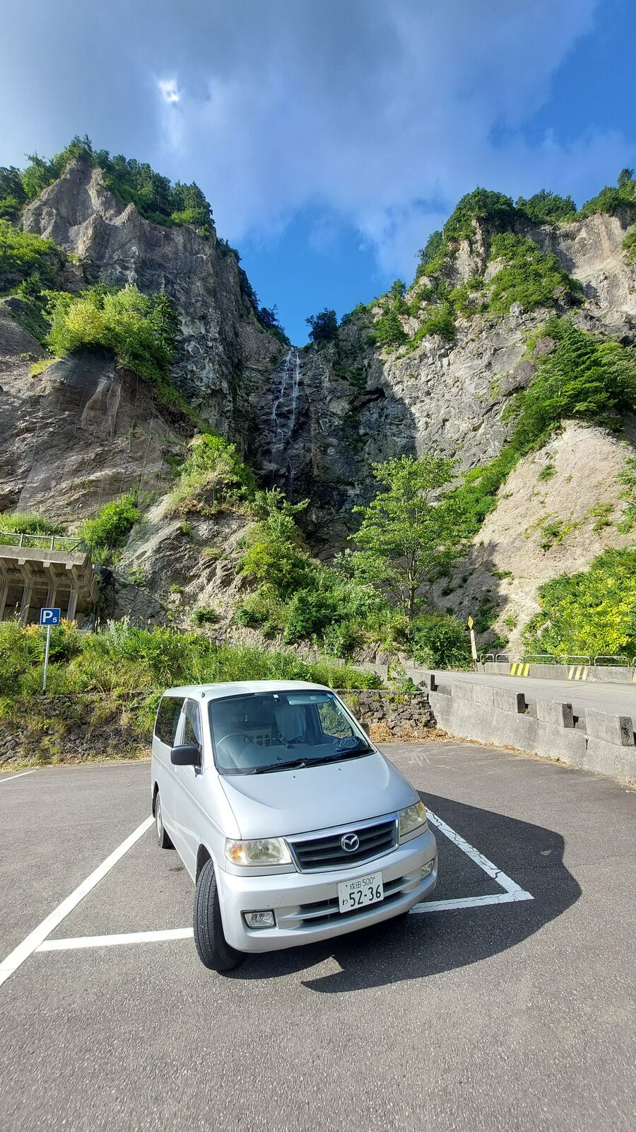 Front view of the campervan against the raw cliff face, showing the scale of the mountain engineering