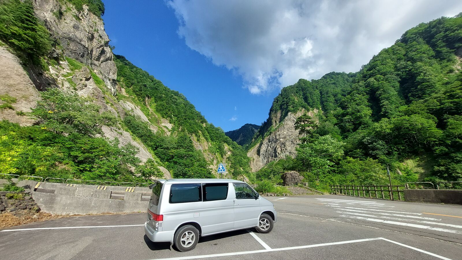 Campervan in the parking area dwarfed by massive exposed rock faces on both sides of the gorge