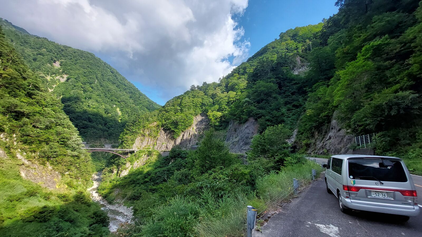 Campervan parked on the roadside with a bridge spanning the gorge in the background, deep green valley and dramatic clouds