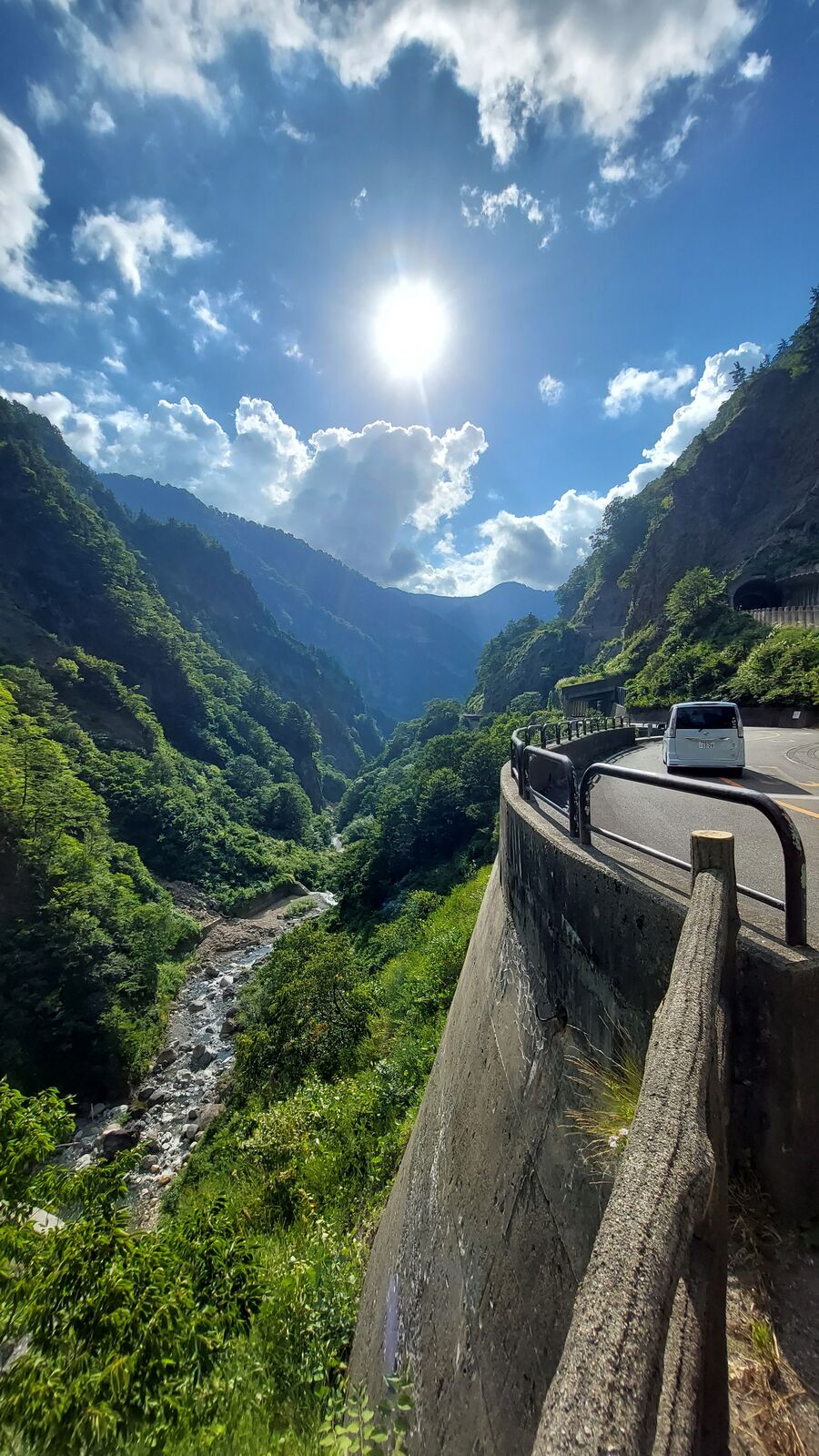 View past the van looking down into the valley with sun flare breaking through the mountain peaks