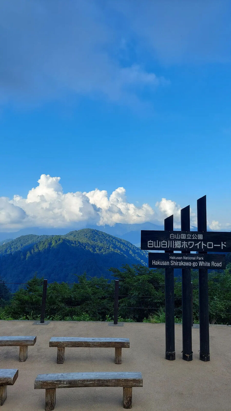 The official Hakusan Shirakawa-go White Road sign at the summit viewpoint with wooden benches and mountains behind