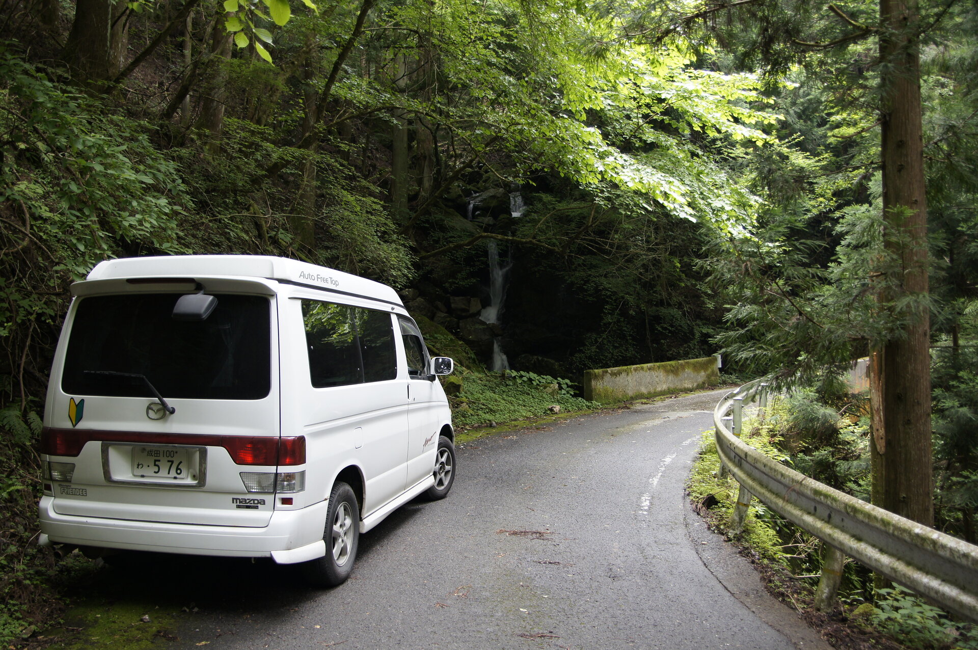Campervan on narrow forest mountain road with waterfall